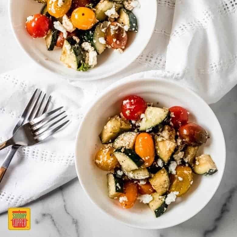two small white bowls with tomato cucumber feta salad