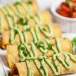 Chicken Taquitos Recipe: chicken taquitos on white platter with fresh avocado crema
