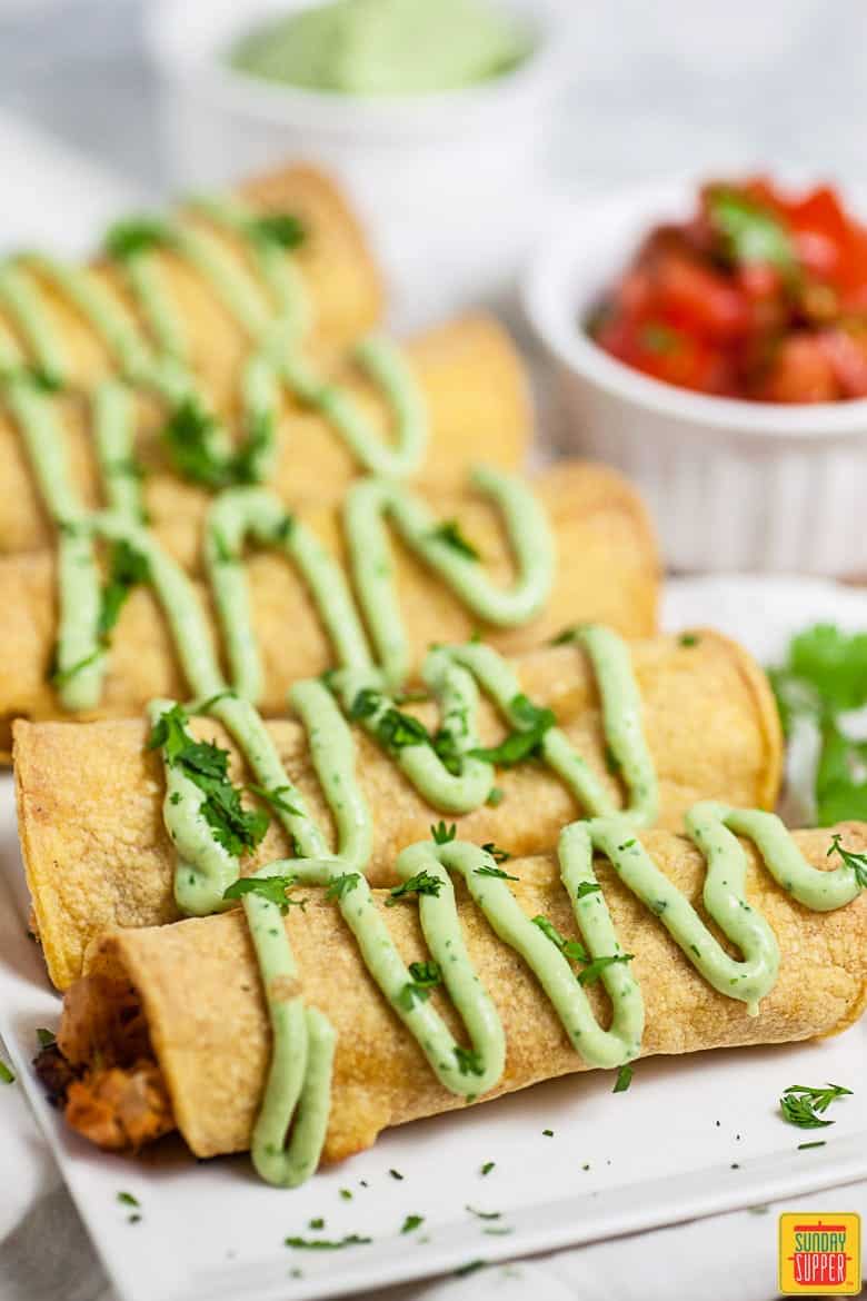 Chicken taquitos on white platter with avocado crema