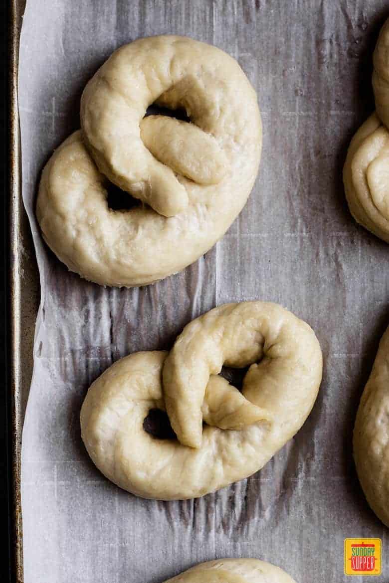 Twisting and preparing dough for soft pretzel recipe on a parchment-lined baking sheet