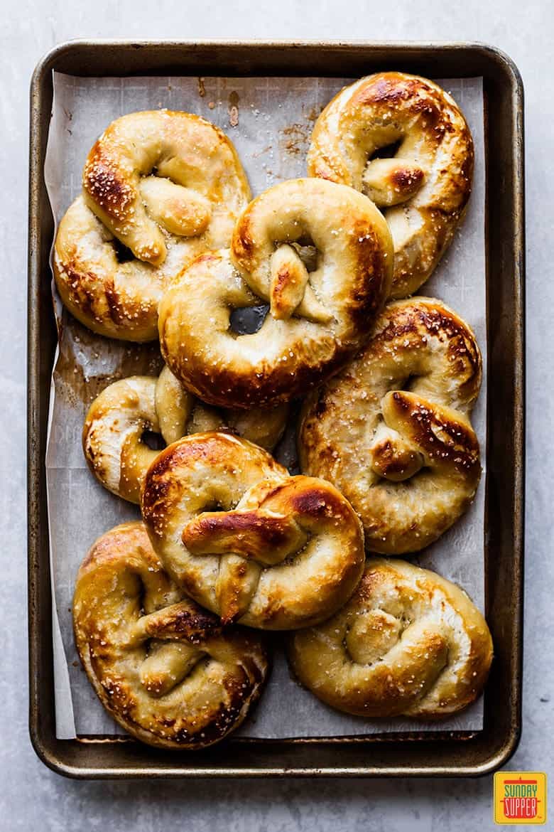 Freshly baked soft pretzel recipe on a parchment-lined baking sheet, stacked on top of each other
