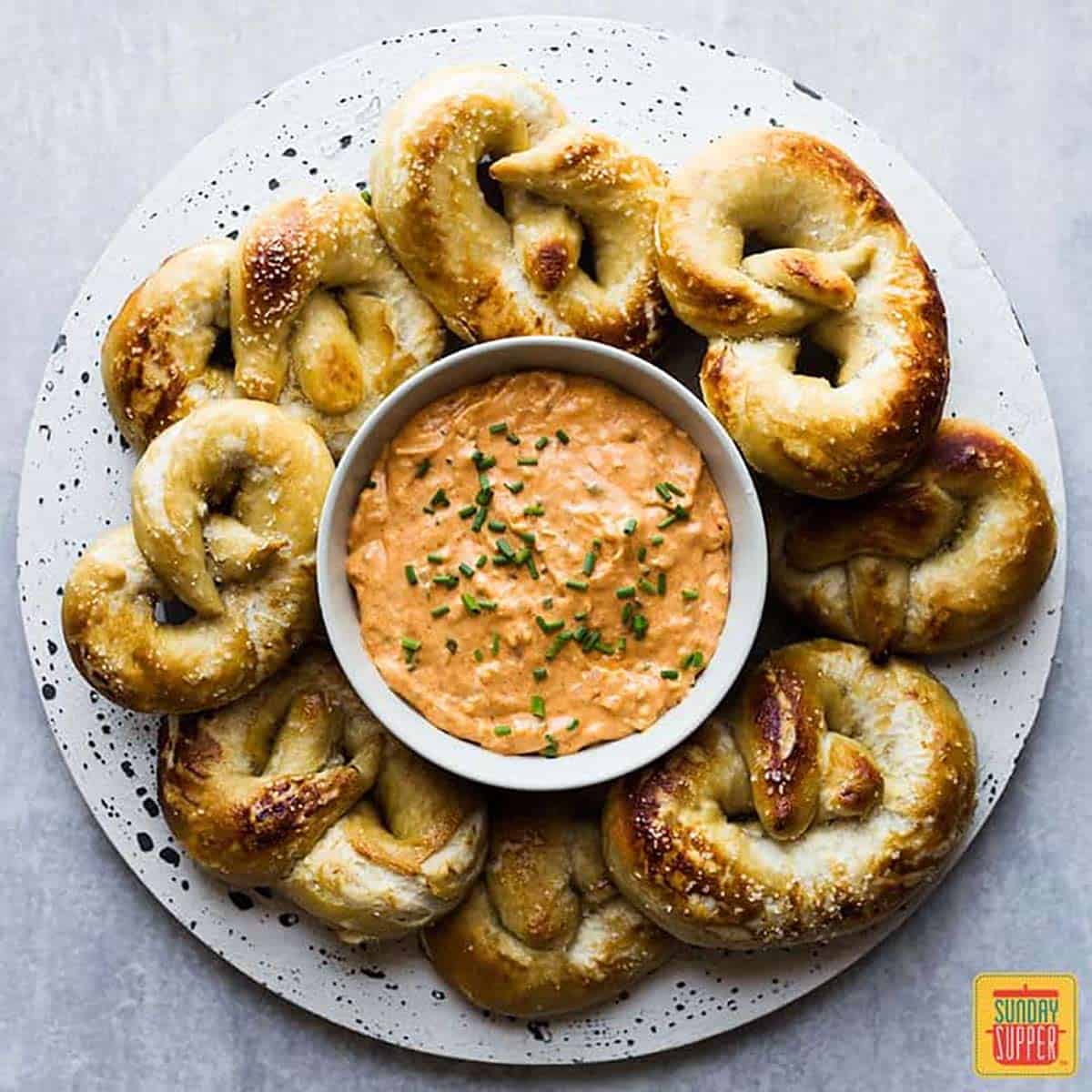 Beer Cheese Dip (Obatzda) in a white dish surrounded by homemade soft pretzels on a white speckled plate