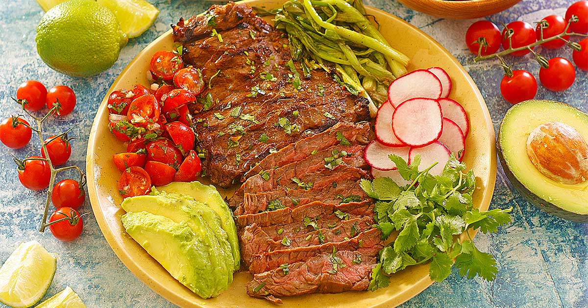 carne asada sliced on a plate with vegetables and avocado