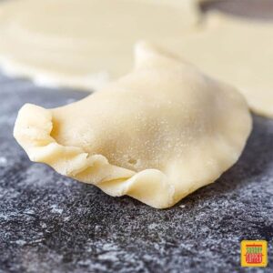An unbaked chicken empanada with the edge crimped slightly to show how to fold empanadas