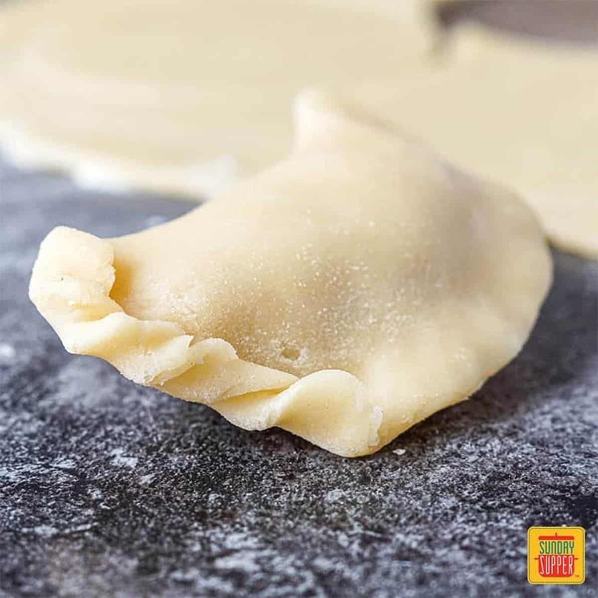 An unbaked chicken empanada with the edge crimped slightly to show how to fold empanadas