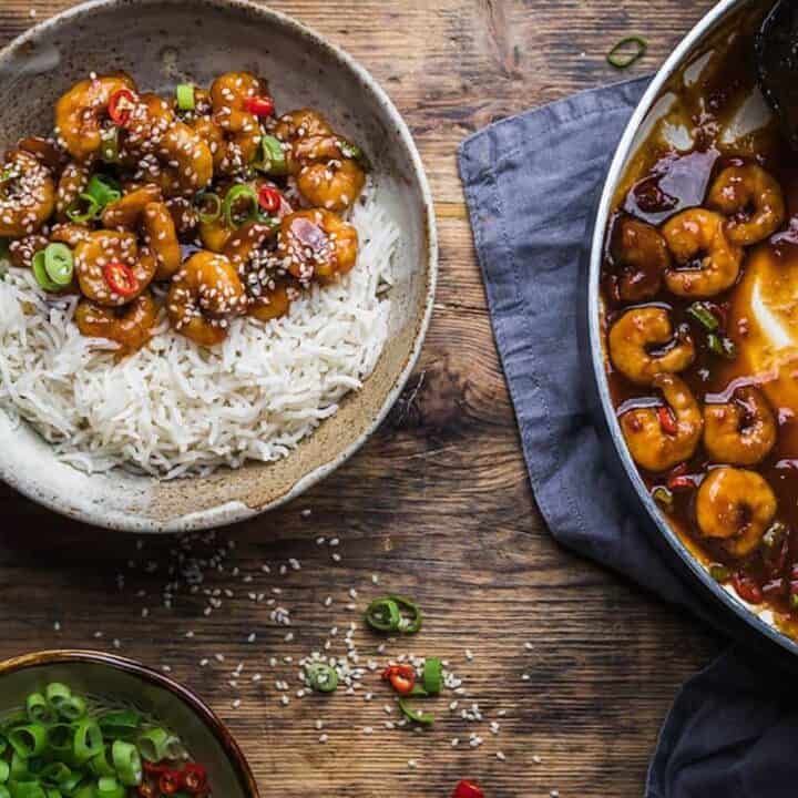 Chinese prawns recipe in a bowl with rice near pan with prawns and sauce