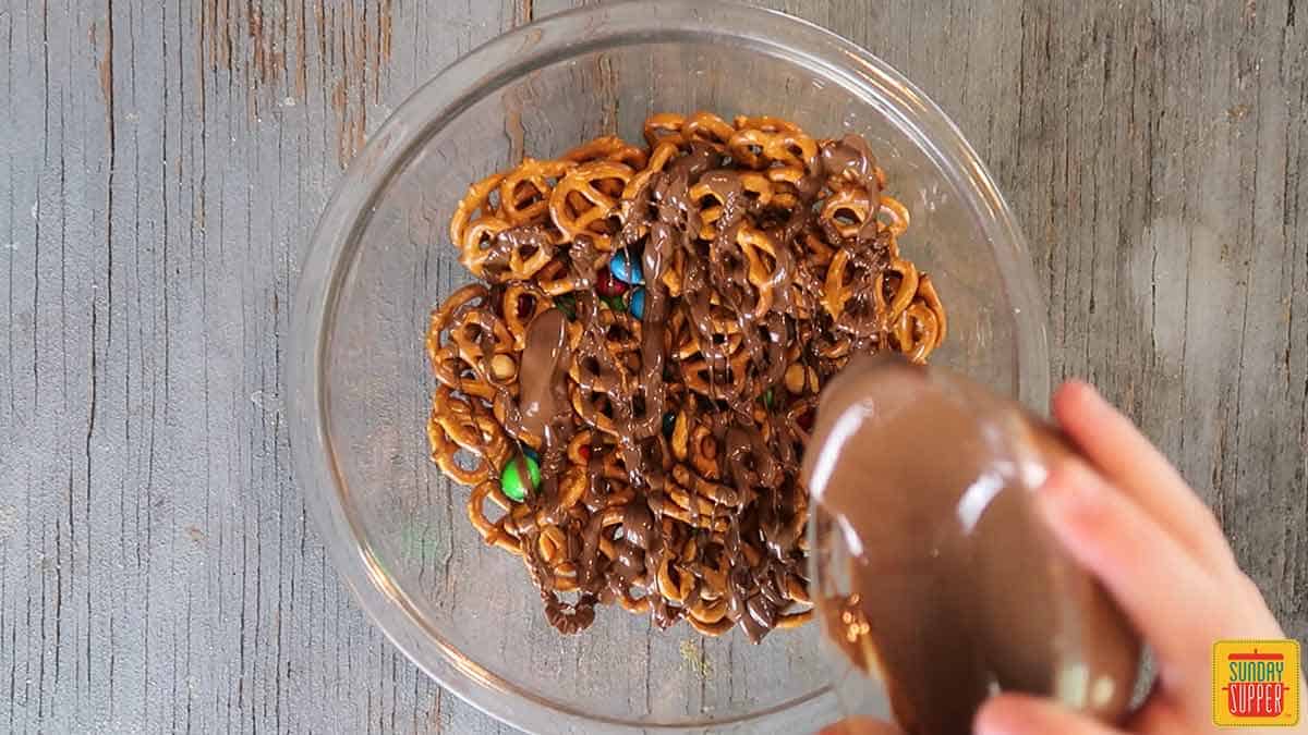 Pouring milk chocolate over peanuts, m&ms, and pretzels