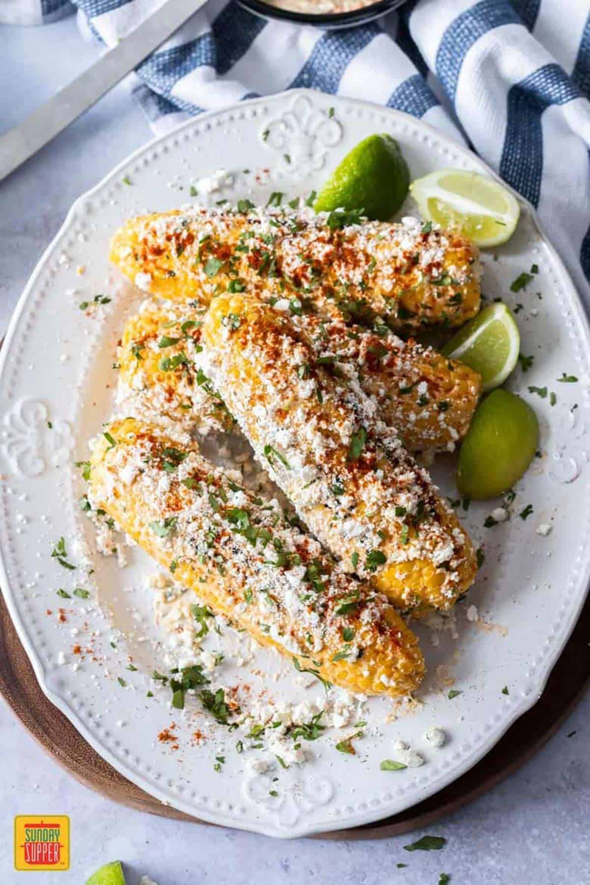 White platter of corn on the cob brushed with Mexican crema