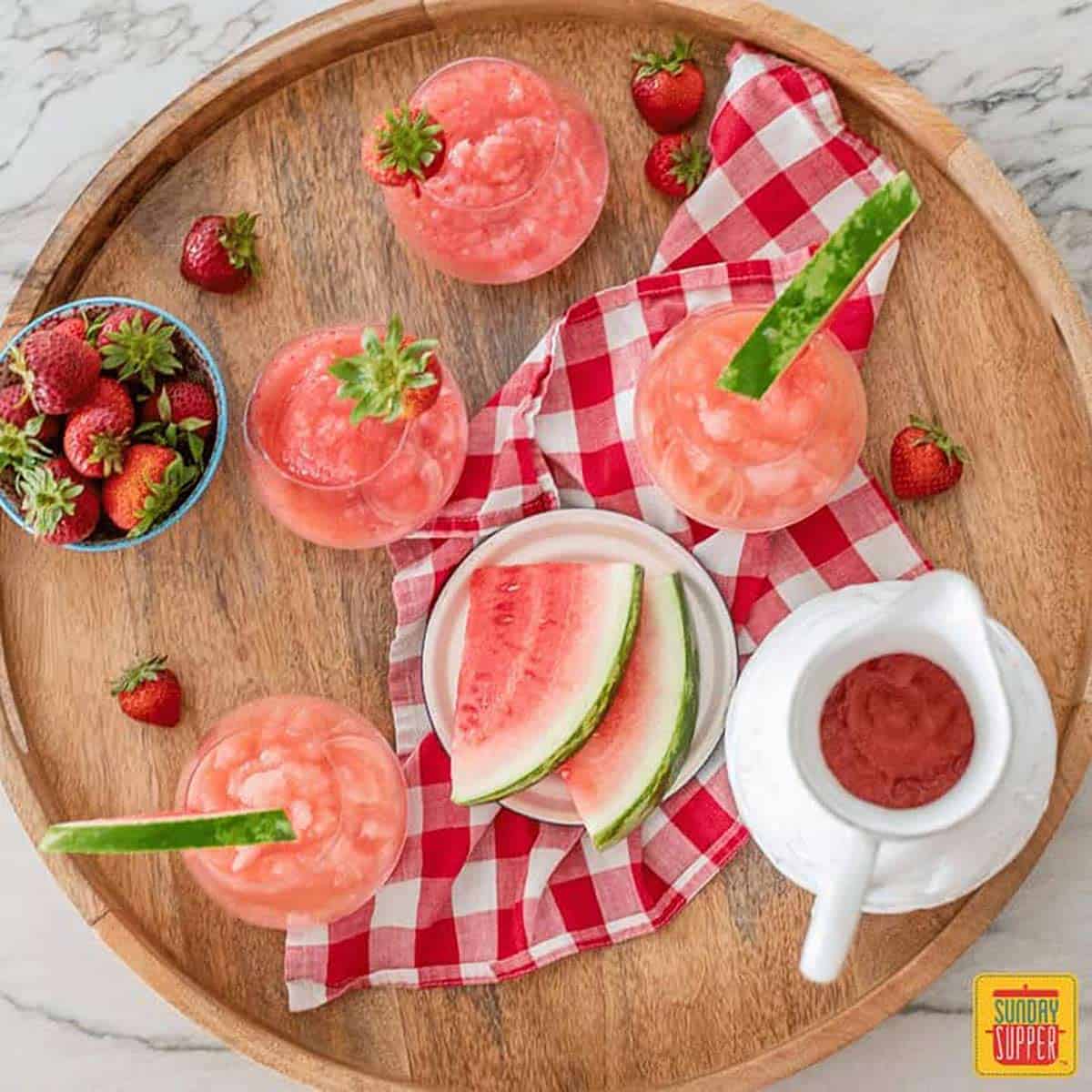 Wooden platter with froze cocktails in glasses and fresh strawberries and watermelon slices