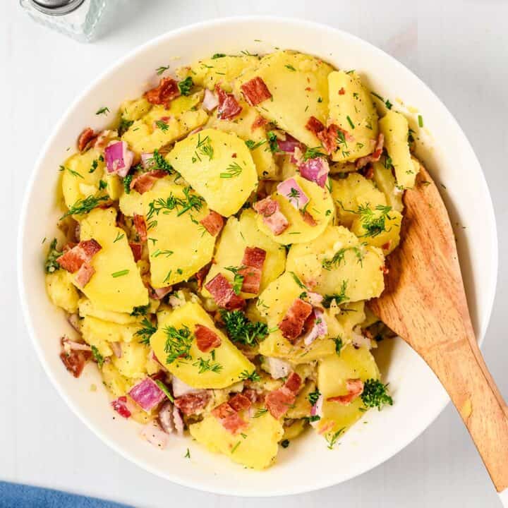 mixing german potato salad in a bowl with a wooden spoon
