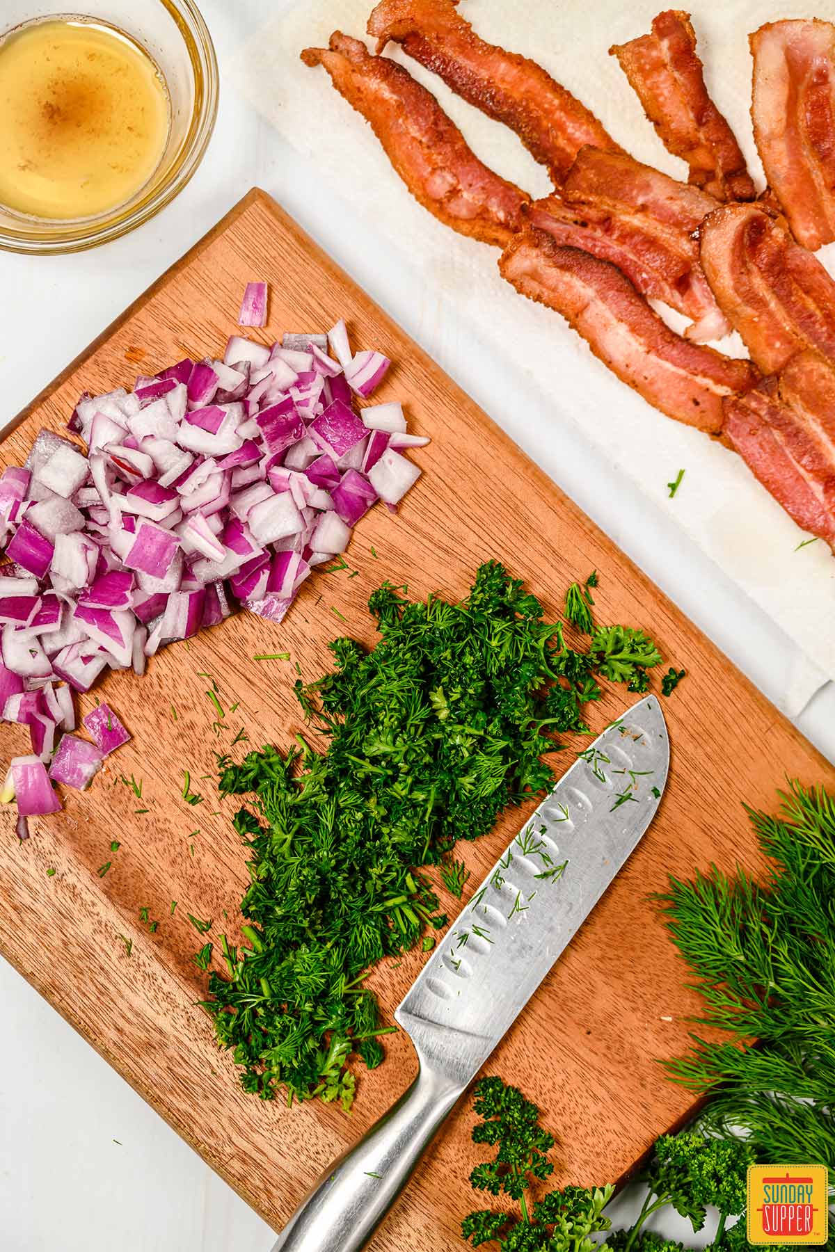 Chopped herbs and onions next to cooked bacon