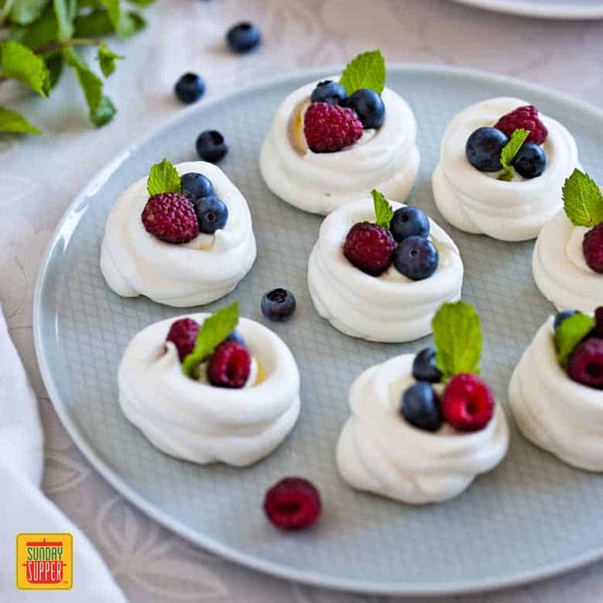 A plate of mini pavlovas with fresh berries and sprigs of mint