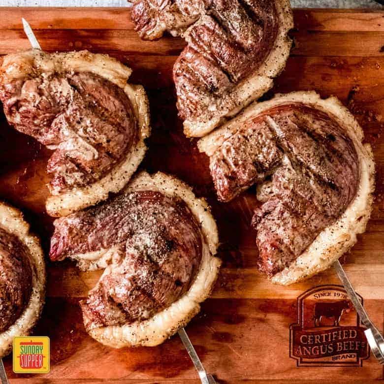 Cooked picanha steak cuts on skewers on a wooden cutting board