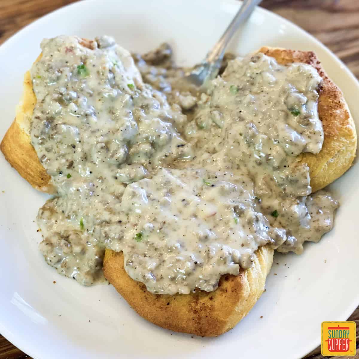 Three biscuits with sausage gravy on top on a white plate