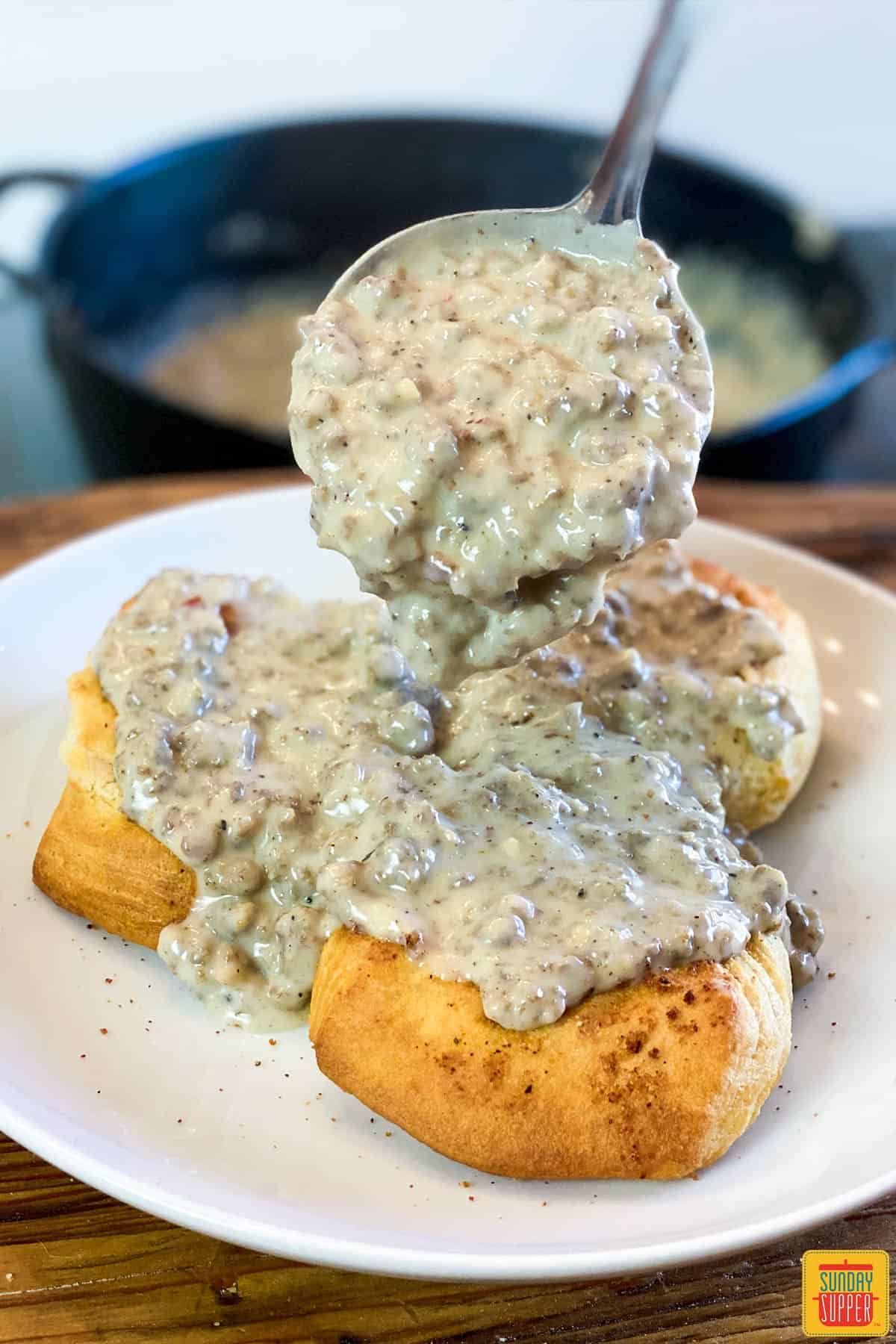 Pouring gravy on sausage biscuits gravy on white plate