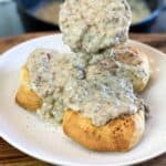 Pouring sausage gravy recipe on three fluffy biscuits