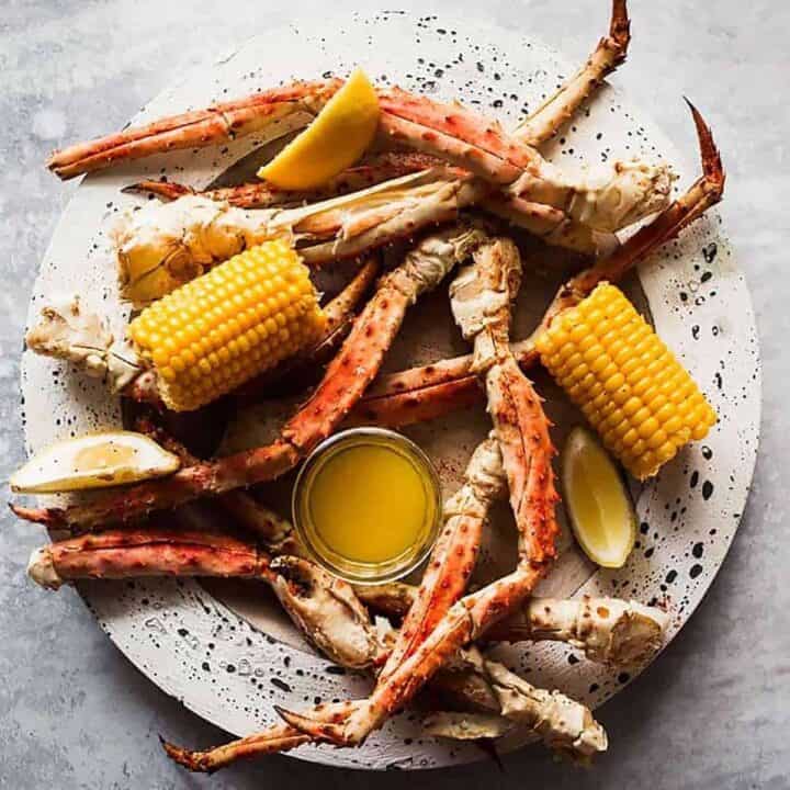 Steamed crab legs on a speckled plate with a glass dish of melted butter and two corn on the cob halves