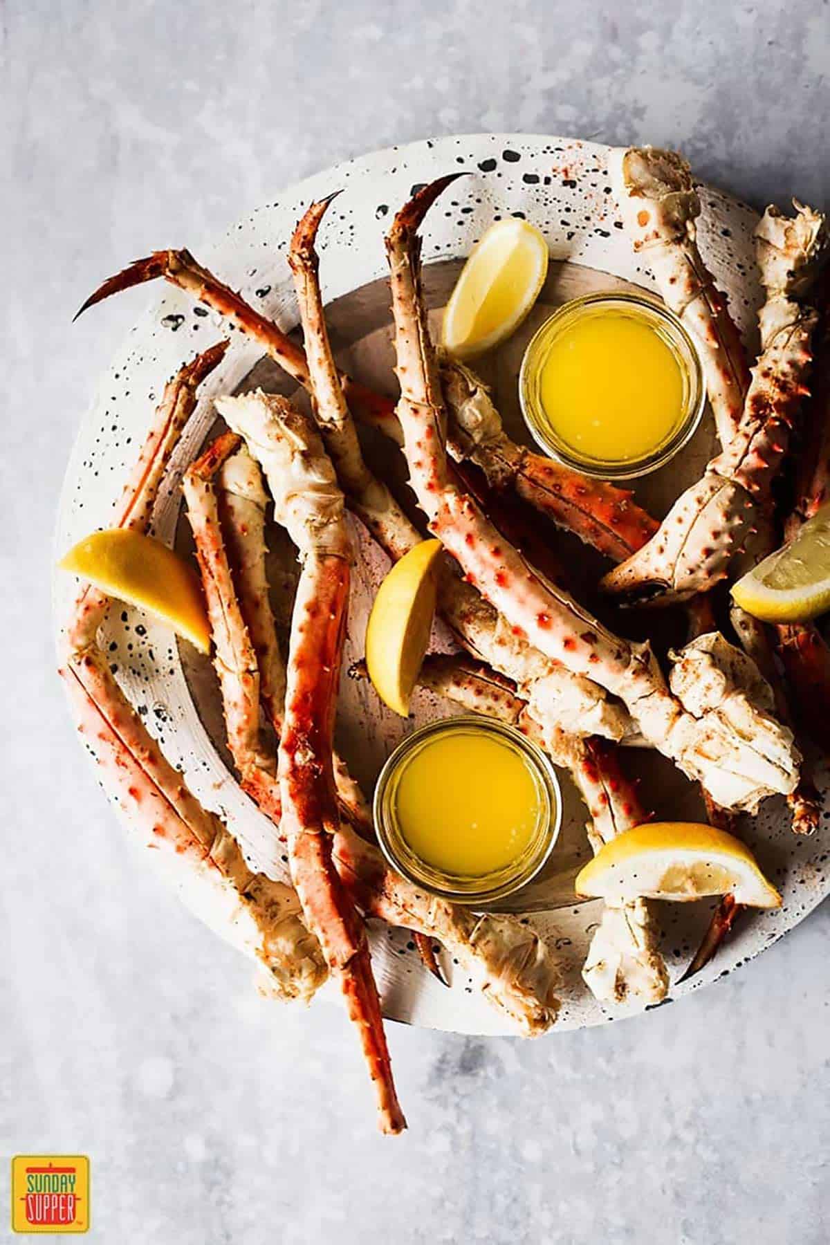 Steamed crab legs on a speckled white plate with lemon garlic butter sauce in dishes