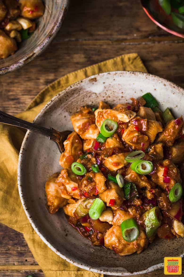 Dragon chicken in a speckled bowl with a fork ready to enjoy, topped with green onions