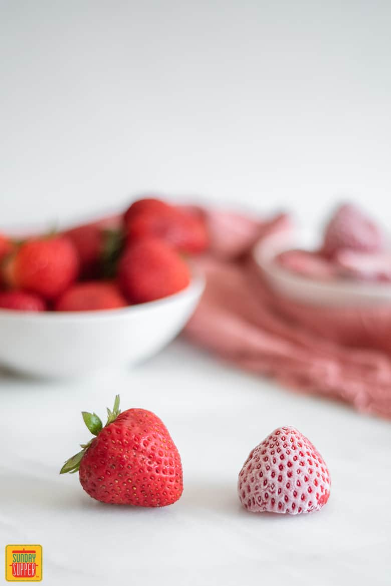 A frozen strawberry next to a fresh strawberry