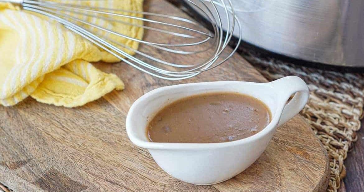 Slow cooker beef gravy in a gravy dish with a whisk nearby