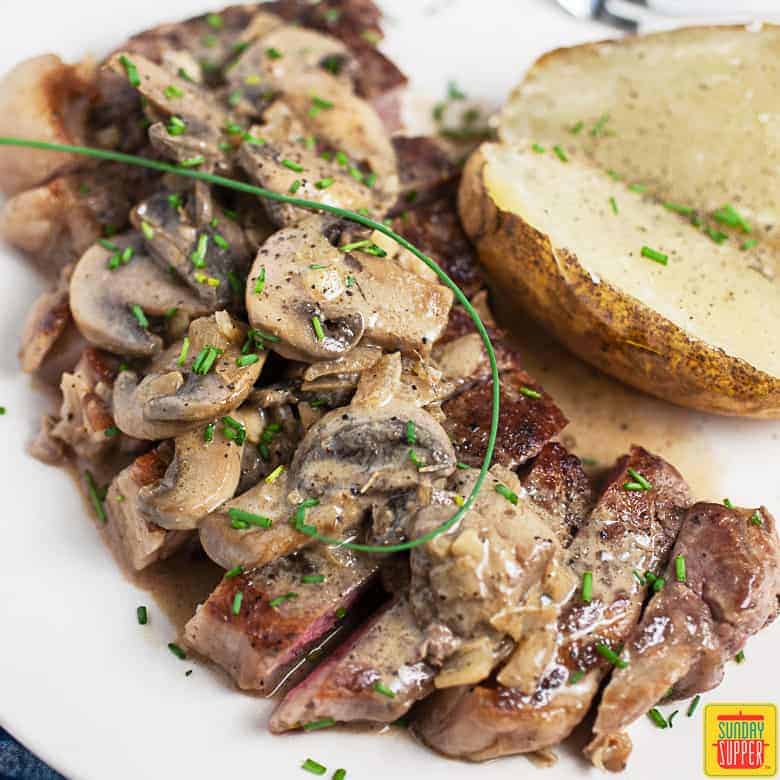 Steak diane recipe on a white dish with baked potato on the side