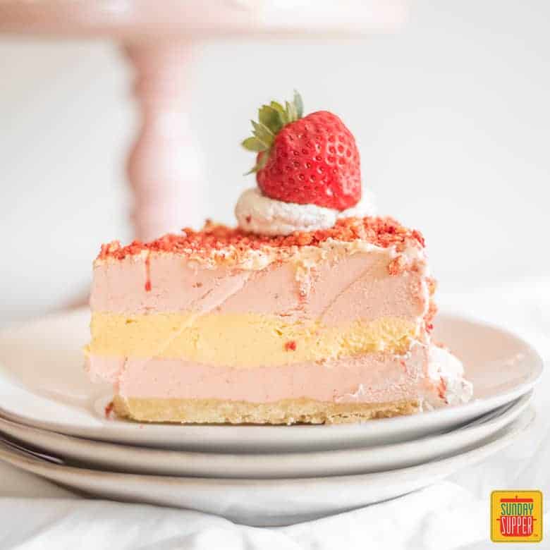 A slice of strawberry ice cream shortcake on two stacked plates with a fresh strawberry on top