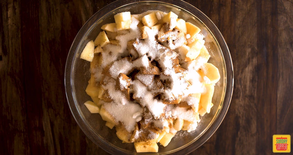 Sugar and spices over diced apples in a glass bowl