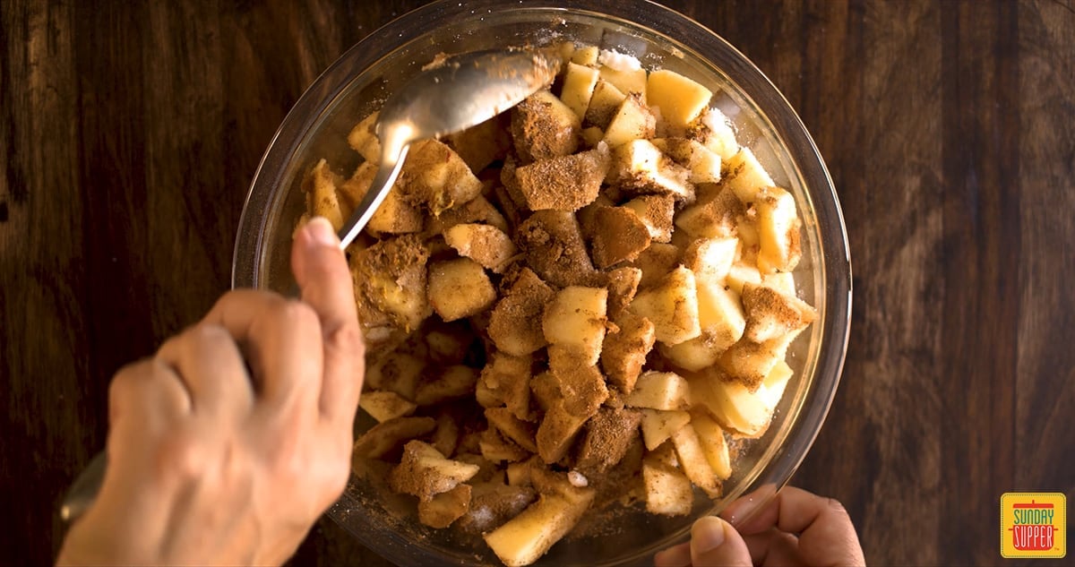 Stirring sugar and spices into diced apples in a glass bowl with a spoon