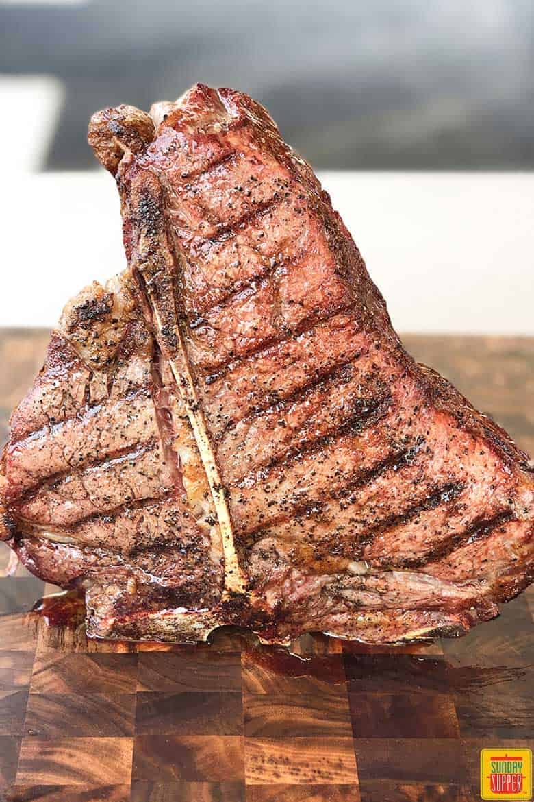 A cooked porterhouse steak balanced to stand up right on a cutting board