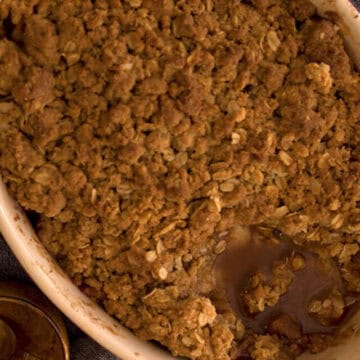 Apple crisp in an oval baking dish next to a slice of apple crisp on a plate with ice cream