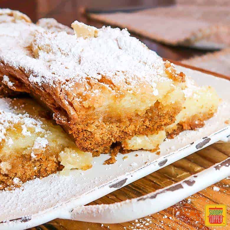 ooey gooey butter cake on a white platter covered in powdered sugar