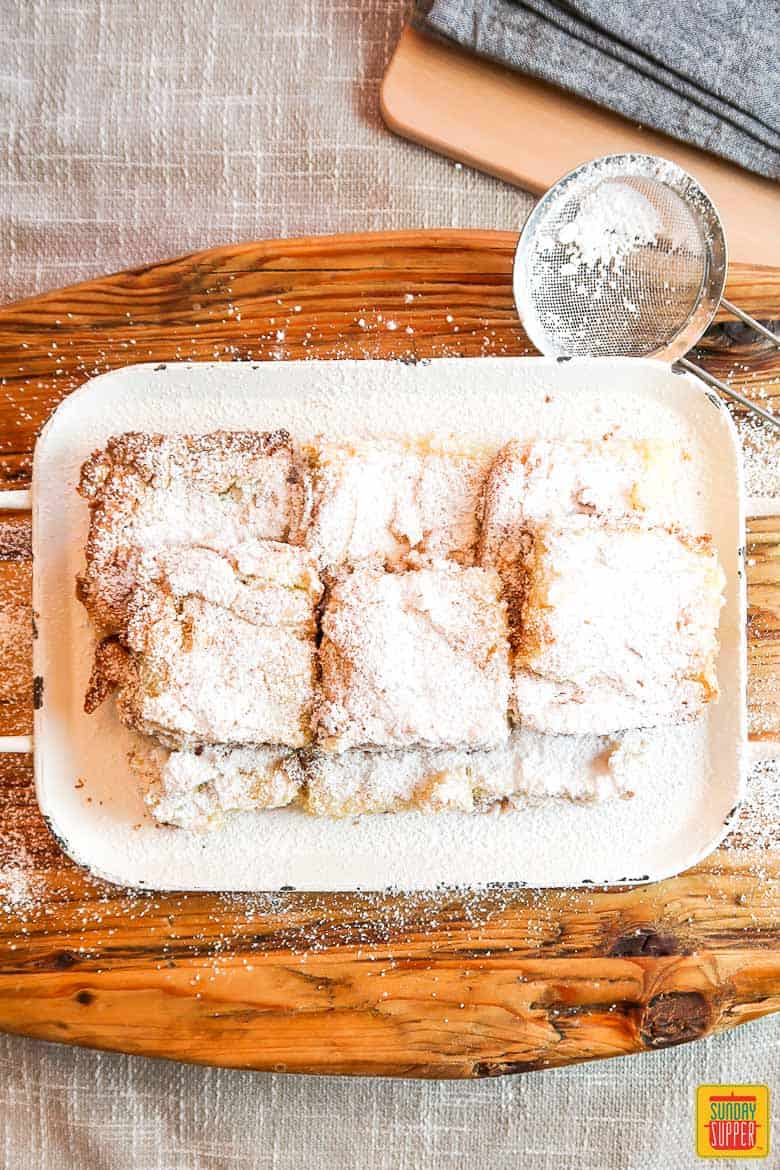Ooey gooey butter cake bars on a white rustic platter sprinkled with confectioners sugar