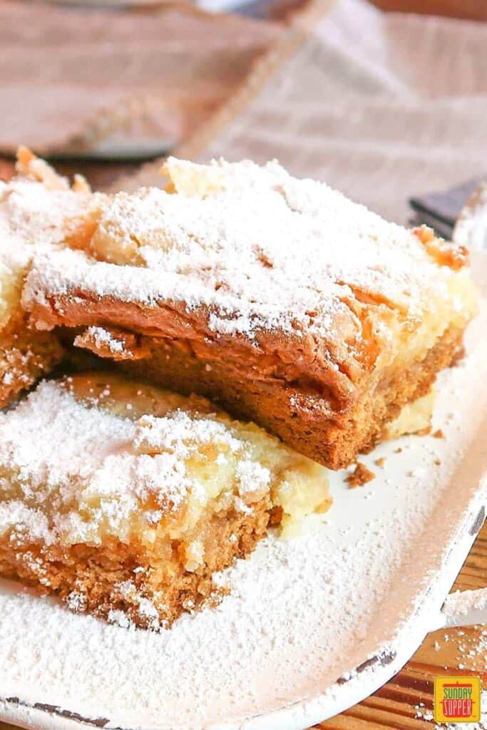 Gooey butter cake bars on a white platter with powdered sugar on top