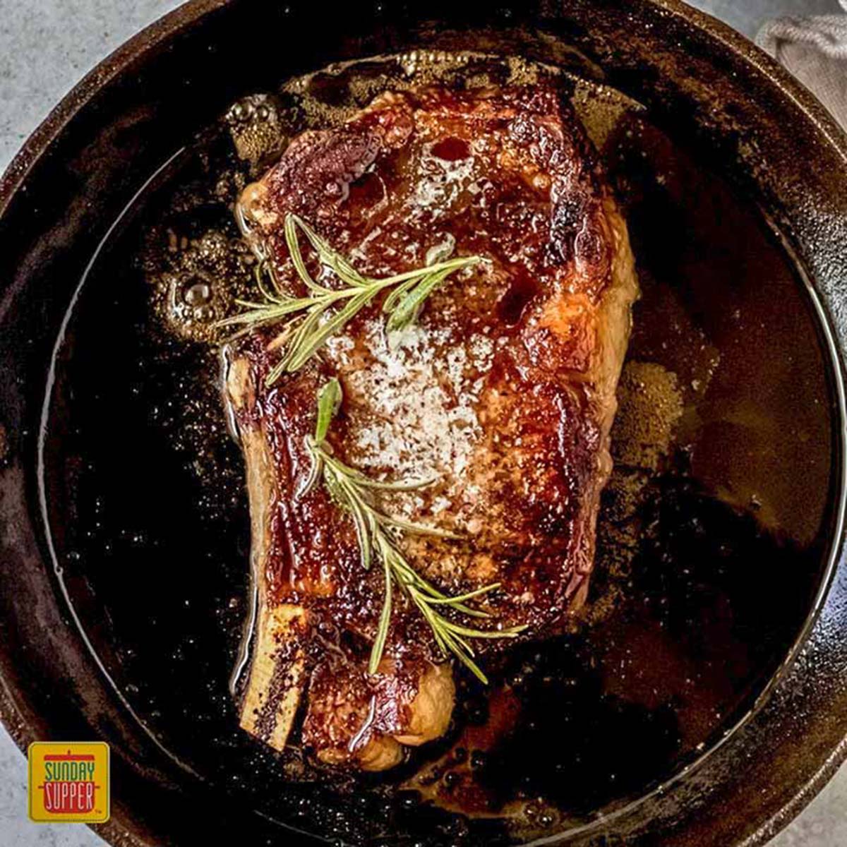 A reverse sear ribeye in a cast iron skillet with fresh herbs on top