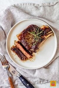 A sliced ribeye steak on a white plate next to a forkk