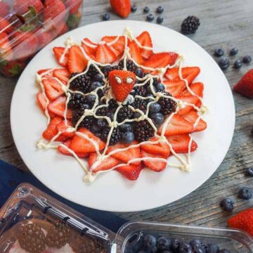 spider-man web berry dessert on white plate surrounded by fresh berries