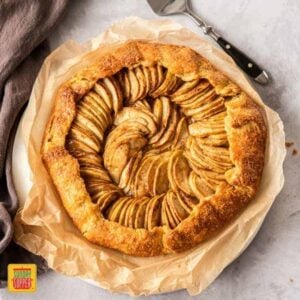 Birdseye view of an apple galette on a sheet of bakign paper. It sits on a concrete background