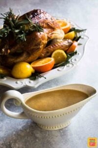 Thanksgiving turkey recipe on a white platter with herbs and citrus next to a gravy boat filled with turkey gravy