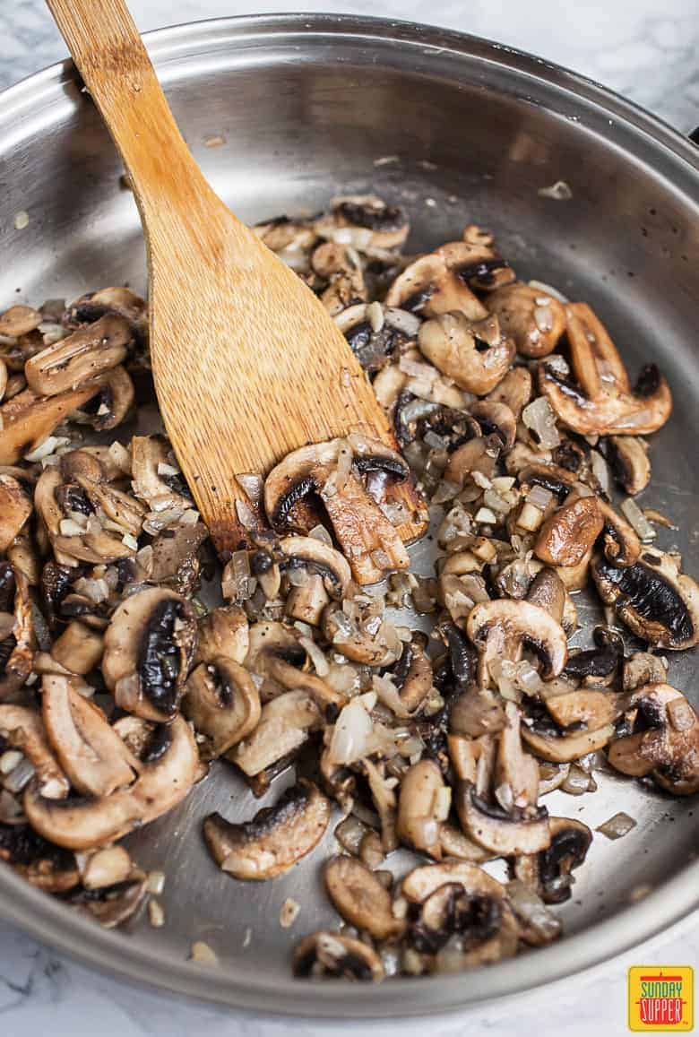 Sauteed Mushrooms In Skillet with a wooden spatula