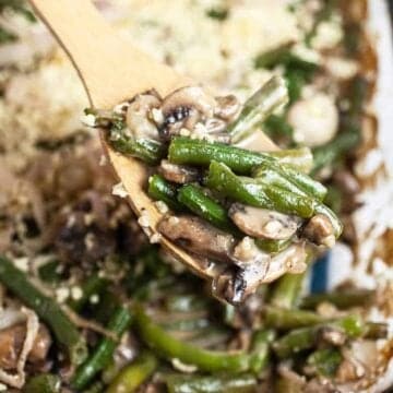 A gluten-free green bean casserole in a glass dish with a wooden serving spoon