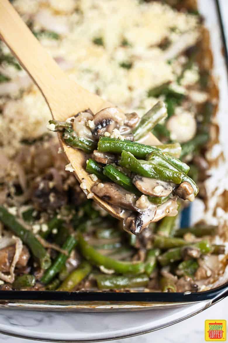 A gluten-free green bean casserole in a glass dish with a wooden serving spoon