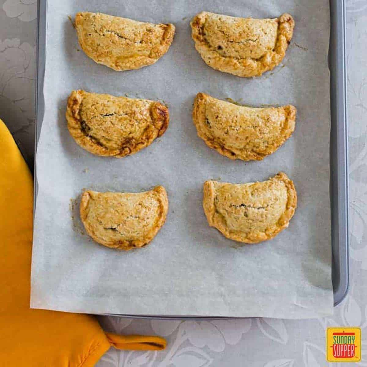 Six pumpkin empanadas on parchment paper on a baking sheet