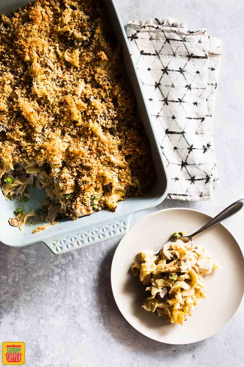 Turkey tetrazzini recipe in a casserole dish next to a plate with a single serving and a fork