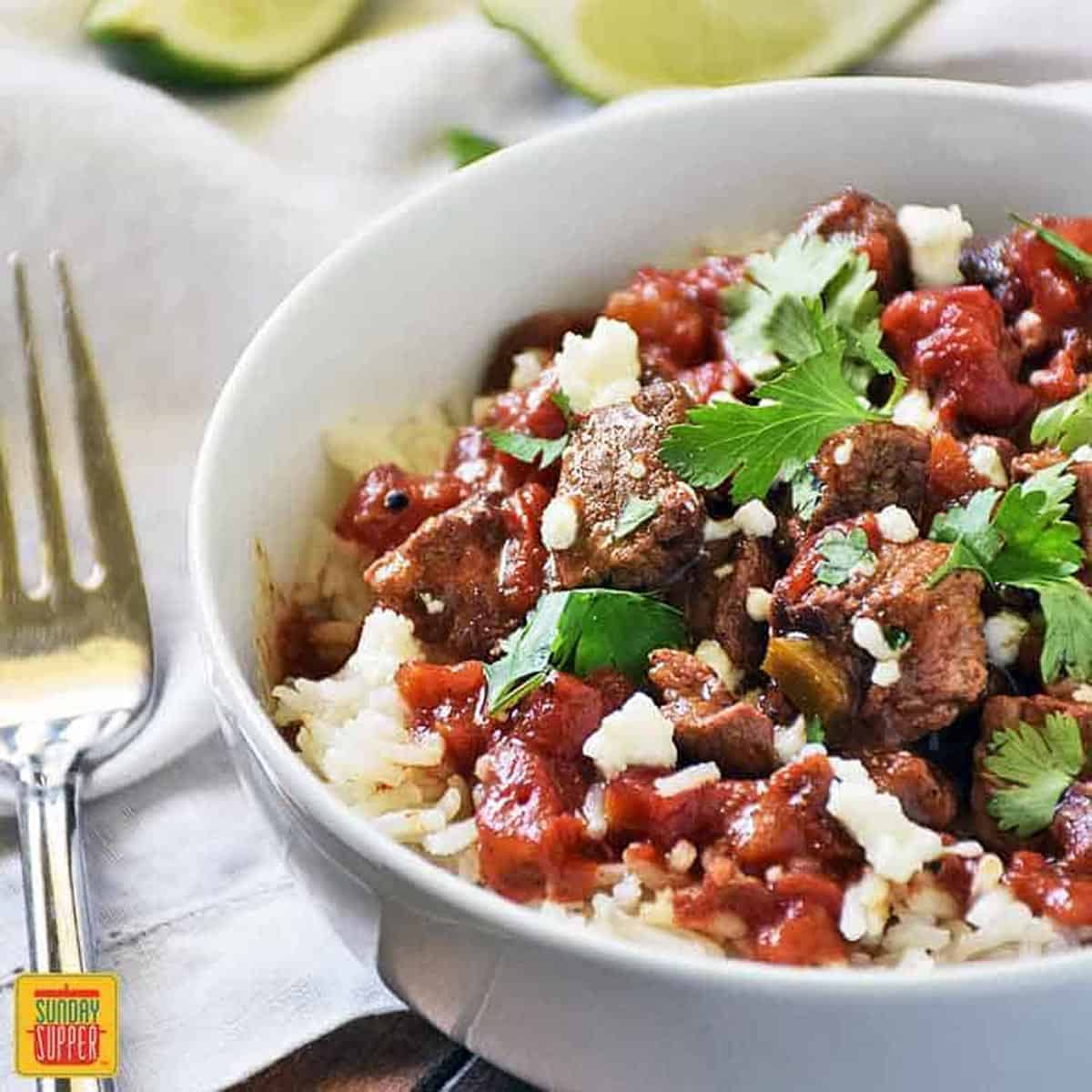 Carne picada slow cooker recipe in a white bowl with a fork to the side and cilantro on top