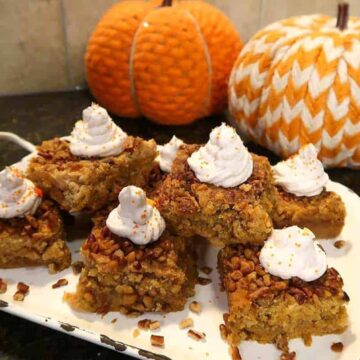 Pumpkin crunch cake bars on a white platter with fabric pumpkins in the background