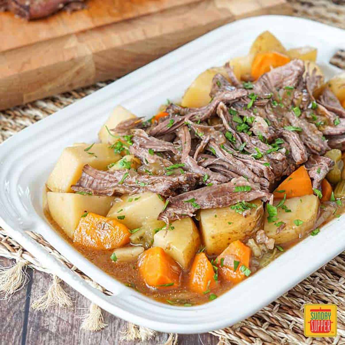 Close up of slow cooker chuck roast on a white platter with potatoes and carrots