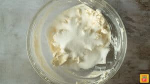Sugar added to cream cheese in a glass bowl