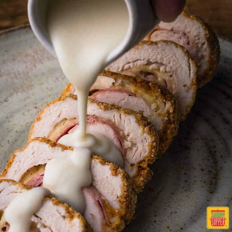 Pouring Parmesan dijon sauce over freshly made Chicken Cordon Bleu recipe