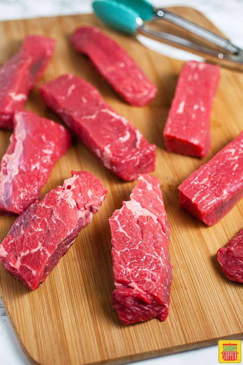 Beef short ribs on a cutting board next to some tongs